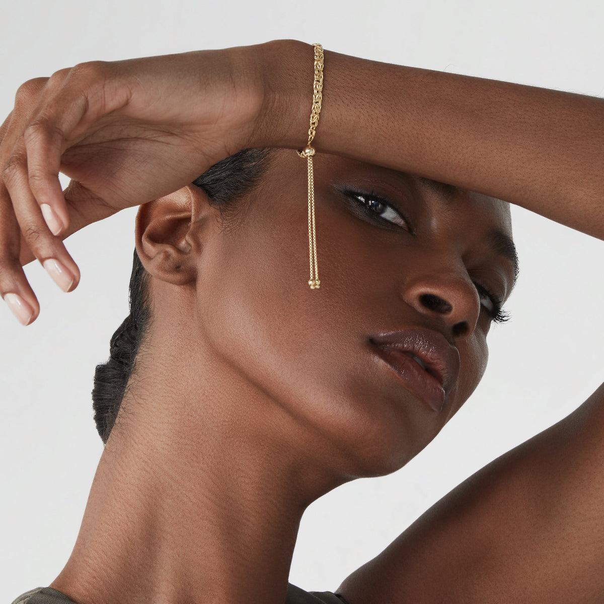 Lifestyle photograph of a model wearing an adjustable gold-tone bolo bracelet with its sliding clasp and two dangling chain ends visible; styling reference, not Suzy Levian jewelry