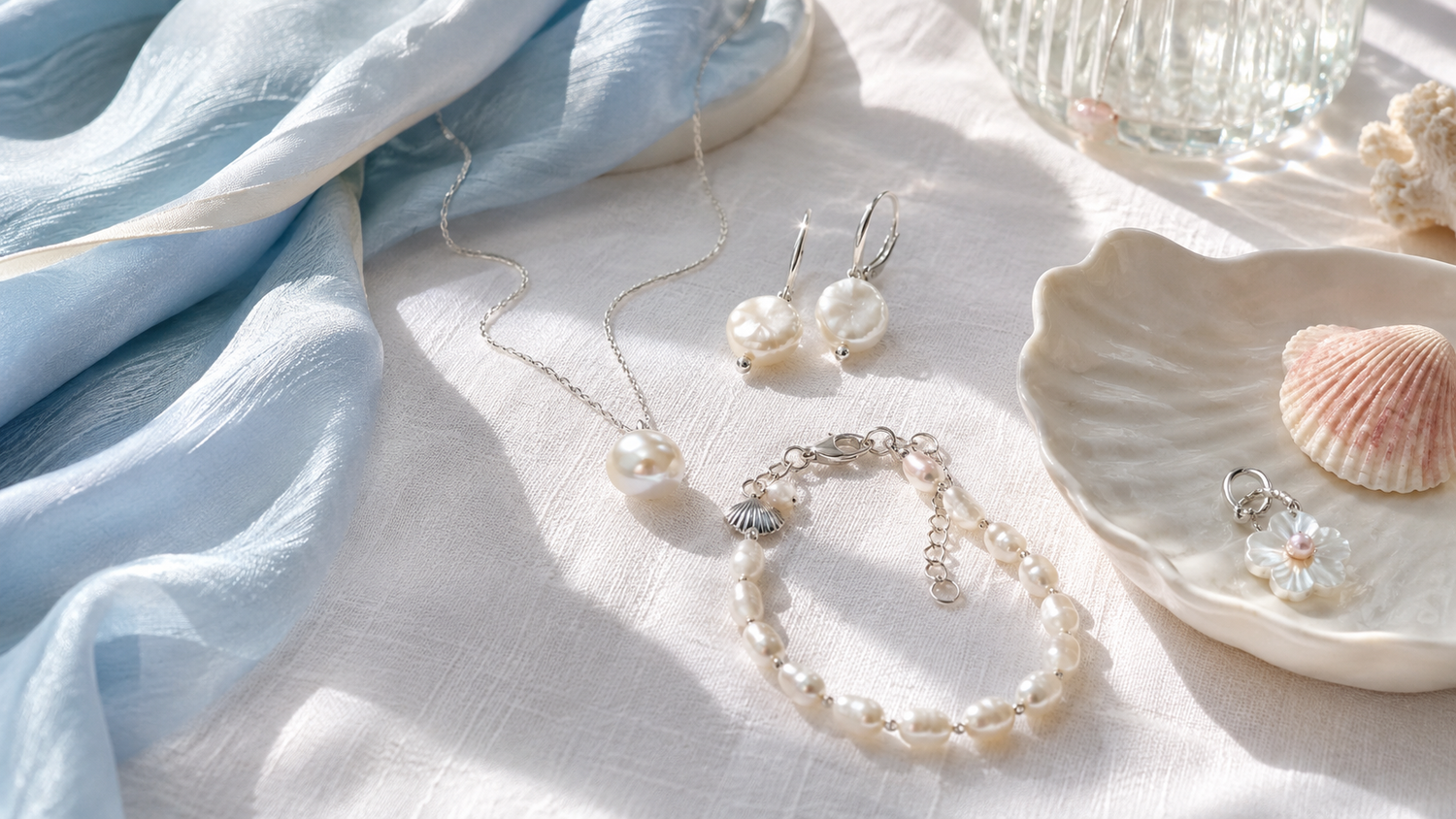 Pearl jewelry styled on white linen with a pale blue scarf and shell dish for a summer 2026 trend story
