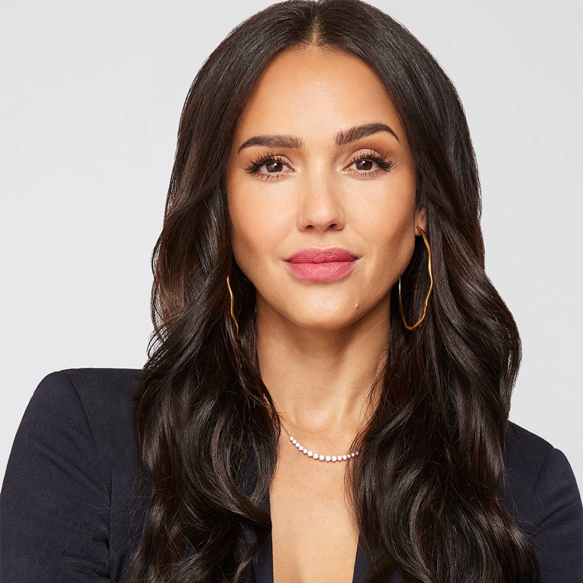 Jessica Alba wearing a black blazer with gold hoop earrings and a delicate necklace in a professional editorial portrait; styling inspiration, not Suzy Levian jewelry