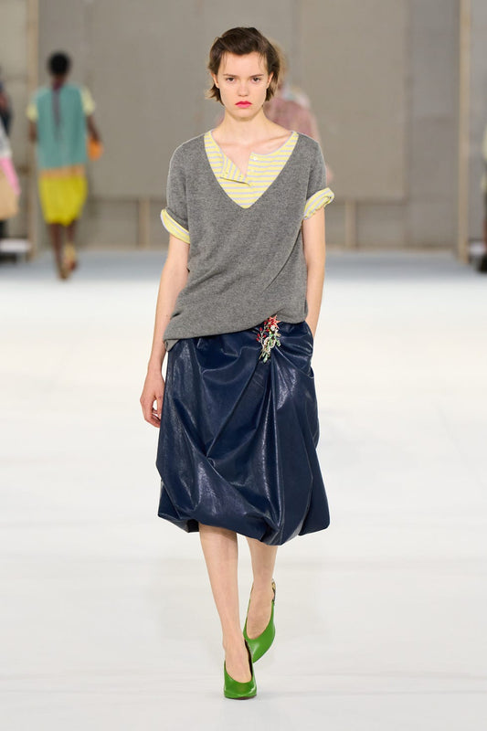 A model wearing a colorful jeweled floral brooch fastened at the waist of a navy skirt during a September 30, 2026 Paris Fashion Week runway show