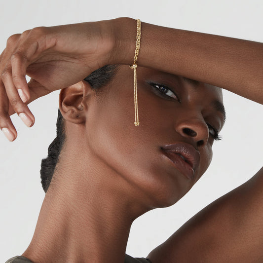 Lifestyle photograph of a model wearing an adjustable gold-tone bolo bracelet with its sliding clasp and two dangling chain ends visible; styling reference, not Suzy Levian jewelry