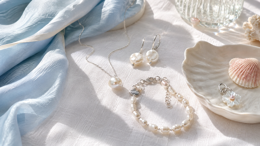 Pearl jewelry styled on white linen with a pale blue scarf and shell dish for a summer 2026 trend story