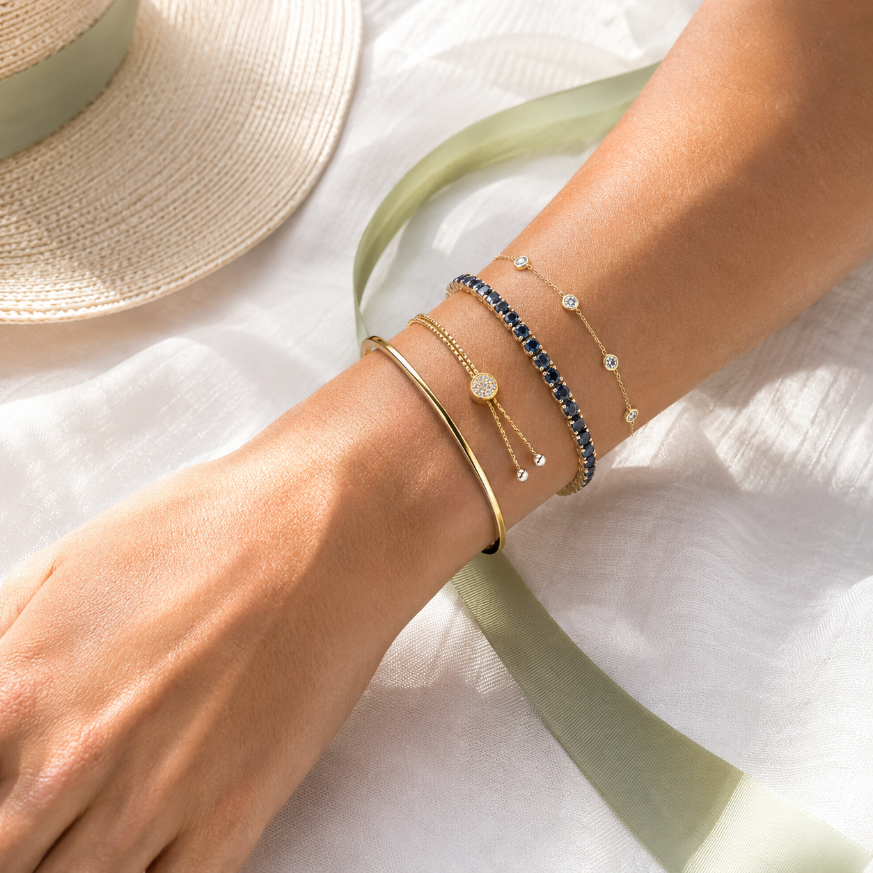 Summer bracelet stack with gold bangle, blue gemstone bracelet, and delicate station bracelets on white linen